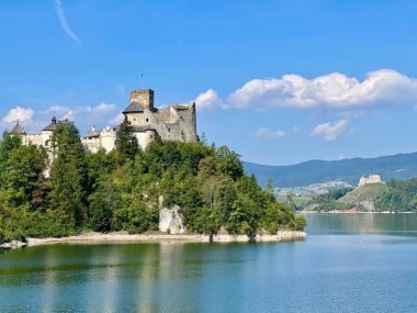 Polonya 'daki Niedzica Kalesi' nin panoramik manzarası. Kale yemyeşil bir yer ve sakin bir göl ile çevrili bir tepeye tünemişti. Ortaçağ yapısında taş duvarlar ve kuleler yer alıyor.