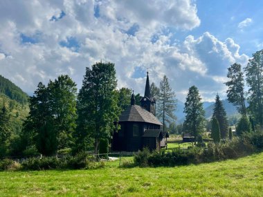 Slovakya 'nın Tatranska Javorina kentindeki kilisenin ve Tatra dağlarının çarpıcı panoramik manzarası. Yoğun orman ve yuvarlanan tepelerle çevrili yemyeşil vadide yuva yapmış ahşap kilise.