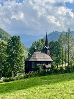 Slovakya 'nın Tatranska Javorina kentindeki kilisenin ve Tatra dağlarının çarpıcı panoramik manzarası. Yoğun orman ve yuvarlanan tepelerle çevrili yemyeşil vadide yuva yapmış ahşap kilise.