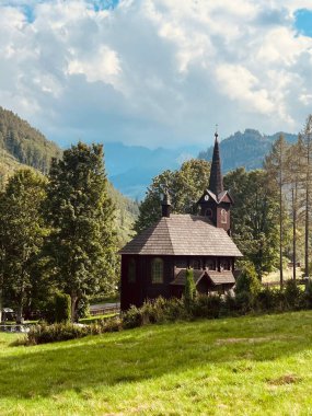 Slovakya 'nın Tatranska Javorina kentindeki kilisenin ve Tatra dağlarının çarpıcı panoramik manzarası. Yoğun orman ve yuvarlanan tepelerle çevrili yemyeşil vadide yuva yapmış ahşap kilise.