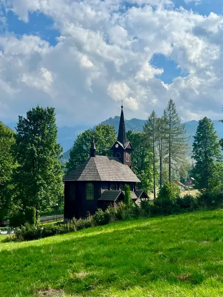 Slovakya 'nın Tatranska Javorina kentindeki kilisenin ve Tatra dağlarının çarpıcı panoramik manzarası. Yoğun orman ve yuvarlanan tepelerle çevrili yemyeşil vadide yuva yapmış ahşap kilise.