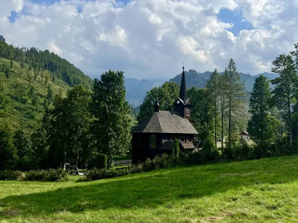 Slovakya 'nın Tatranska Javorina kentindeki kilisenin ve Tatra dağlarının çarpıcı panoramik manzarası. Yoğun orman ve yuvarlanan tepelerle çevrili yemyeşil vadide yuva yapmış ahşap kilise.