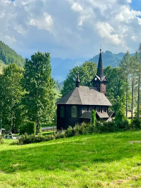 Slovakya 'nın Tatranska Javorina kentindeki kilisenin ve Tatra dağlarının çarpıcı panoramik manzarası. Yoğun orman ve yuvarlanan tepelerle çevrili yemyeşil vadide yuva yapmış ahşap kilise.
