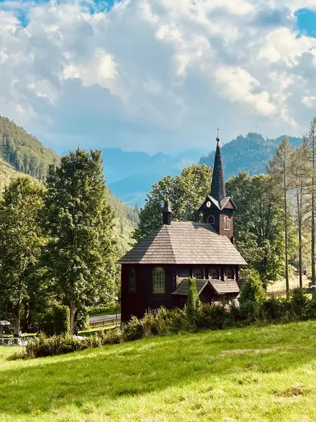 Slovakya 'nın Tatranska Javorina kentindeki kilisenin ve Tatra dağlarının çarpıcı panoramik manzarası. Yoğun orman ve yuvarlanan tepelerle çevrili yemyeşil vadide yuva yapmış ahşap kilise.