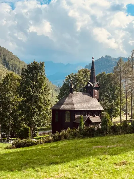 Slovakya 'nın Tatranska Javorina kentindeki kilisenin ve Tatra dağlarının çarpıcı panoramik manzarası. Yoğun orman ve yuvarlanan tepelerle çevrili yemyeşil vadide yuva yapmış ahşap kilise.
