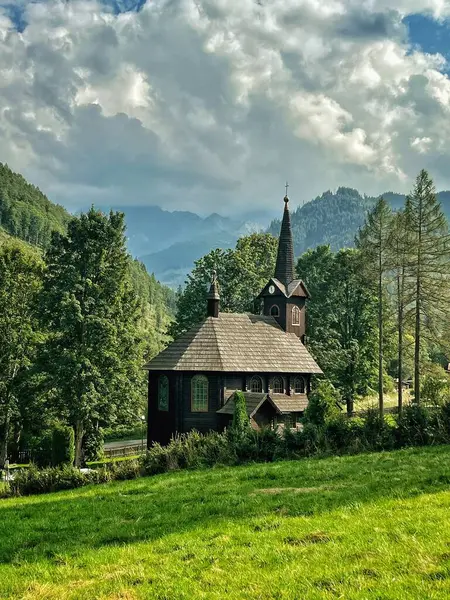 Slovakya 'nın Tatranska Javorina kentindeki kilisenin ve Tatra dağlarının çarpıcı panoramik manzarası. Yoğun orman ve yuvarlanan tepelerle çevrili yemyeşil vadide yuva yapmış ahşap kilise.