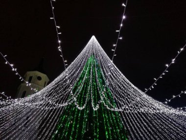 Yeşil koni şekilli ve Litvanya 'nın Vilnius kentindeki bir gölgeliğe benzeyen beyaz ışık dizileriyle aydınlatılmış Noel ağacı kurulumu 