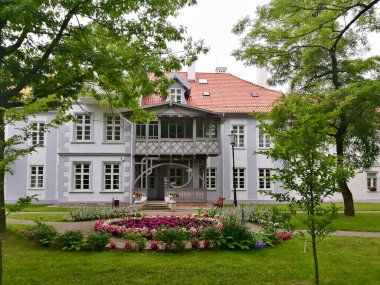 Hugo Scheu Malikanesi Silute, Litvanya 'da. Açık gri ve beyaz simetrik perdeli iki katlı bir malikane. Binada kırmızı kiremitli gablı çatı ve çok sayıda beyaz çerçeveli pencere yer alıyor..