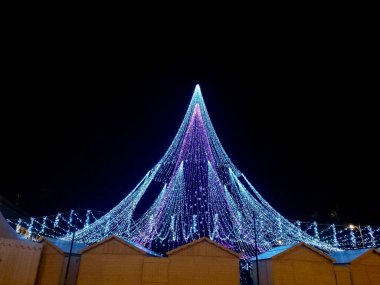 Yeşil koni şekilli ve Litvanya 'nın Vilnius kentindeki bir gölgeliğe benzeyen beyaz ışık dizileriyle aydınlatılmış Noel ağacı kurulumu 