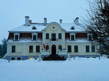 Letonya 'daki Jaunsvente Malikanesi karla çevrili, merkezi girişi belirgin, kıvrımlı çatısı olan klasik mimari tasarıma sahip.