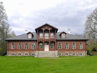 Geniş, ahşap bir Vilkiskes malikanesi, simetrik cepheli, koyu metal bir çatısı ve birden fazla beyaz çerçeveli penceresi var. Merkezi bölümde dekoratif bir balkon ve süslü ahşap kaplama var. Litvanya 