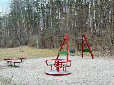 Modern çocuk oyun parkı bir orman ile çevrili kırmızı ve yeşil bir atlıkarınca, iki salıncaklı bir salıncak ve bir tahterevalli. 