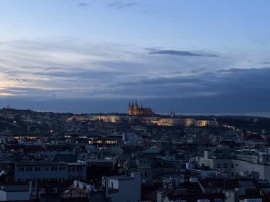Terastan Prag 'ın panoramik görüntüsü. Şehir manzarası aydınlanmış bir alacakaranlık. Prag Kalesi akşam gökyüzüne karşı görünür bir şekilde aydınlanır.. 
