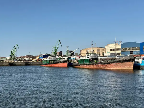 Klaipeda Limanı. Vinçler bir limanın endüstriyel manzarasına hakimdir. Rıhtım boyunca birkaç yeşil vinç duruyor, bazı yapılar ve makineler görülebilir.. 