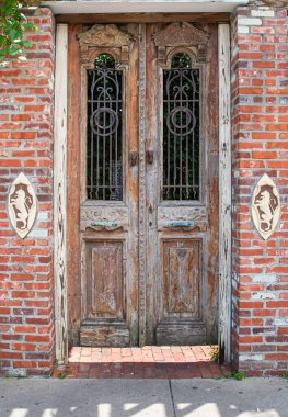 Dekoratif girişi olan tuğlalarla çevrili antik çift kapı. Kapı yıpranmış ve camları parmaklıklı.