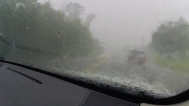 Şiddetli bir fırtınada dört şeritli bir şehir caddesinde araba kullanmak. Silecekler açık ve trafik saatte 25 mil hızla ilerliyor..