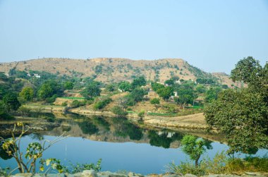 Bir tepenin yansıması ve dalgalanmasız temiz suyu olan küçük bir göldeki ağaçlar.