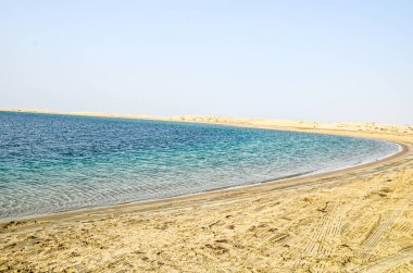 Katar 'daki Al-Adaid Çölü' nün arka planında kireçtaşı tepeleri olan kum tepeleri dereye iniyor.