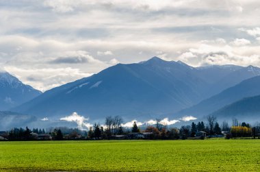 Kanada 'nın Abbotsford' dan Umut 'a giden otobandaki kırsal manzarası. Kanada' da kar kaplı dağlar, alçak seviye bulutlar, vadiler ve tarlalar arka planda.