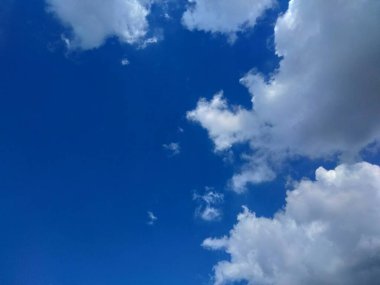 Gökyüzü açık mavi, dağınık beyaz bulutlar sakin ve huzurlu bir atmosfer yaratıyor..