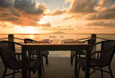 Table with glasses in restaurant, Beau Vallon Beach, Island Mahe, Republic of Seychelles, Africa.   Table with glasses in restaurant with view of sunset. Island Silhouette in the background. 