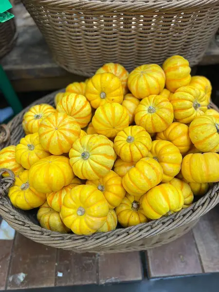 Sonbahar hasadının canlı bir gösterisini sergileyen küçük sarı balkabaklarıyla dolu bir hasır sepet. Balkabakları düzgünce dizilmiş, parlak renklerini gösteriyorlar..