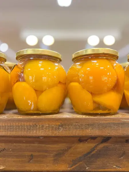 İki şeftali kavanozu, sarı meyvelerin canlı rengini gösteriyor. Yumuşak ışıkla bulanık arka plan şeftalilerin tazeliğini ve dokusunu ön plana çıkarıyor. Sıcaklık ve ev yapımı bir tat yaratıyor..