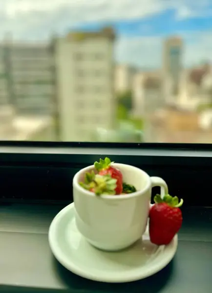 Taze çilekle kaplanmış güzel bir çilek kreması modern bir şehre bakan bir masada beyaz bir fincanda servis edilir. Şehir manzarası arka planda binalar ve bulutlu mavi bir gökyüzü ile ortaya çıkar, bir huzur hissi verir ve 