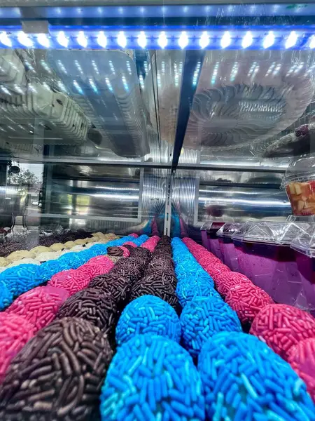 Renkli bir takım tugaylar şık bir şekilde sergileniyor, pembe, mavi ve çikolatanın canlı tonlarında tatlılar sergiliyorlar. Görüntü, neşeli ve davetkar bir ortamda neşe ve cazibe uyandıran zengin dokuları ve parlaklığı vurgular..