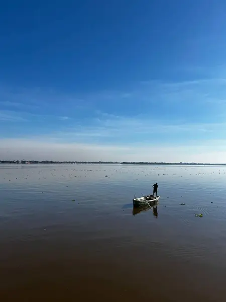 Küçük bir kanodaki yalnız bir balıkçı, berrak bir mavi gökyüzünün altında sakin bir göl boyunca süzülerek suyun güzelliğini ve doğal manzaranın sükunetini yansıtır..
