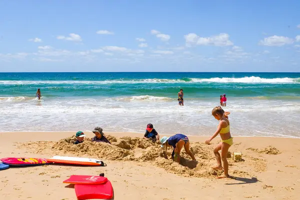 Mavi gökyüzü, güneşli bir gün ve Sunshine Coast 'ta kumla oynayan çocuklar. 