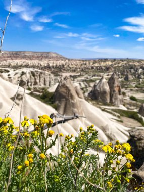 Büyüleyici ve eşsiz doğa ve kaya oluşumunun hava ve panoramik görüntüsü, Kapadokya 'nın peri bacaları, Goreme, Türkiye' nin güzel bir bahar günü mavi gökyüzü, sarı kır çiçeklerinin açtığı