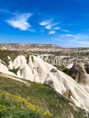 Büyüleyici ve eşsiz doğa ve kaya oluşumunun hava ve panoramik görüntüsü, Kapadokya 'nın peri bacaları, Goreme, Türkiye' nin güzel bir bahar günü mavi gökyüzü, sarı kır çiçeklerinin açtığı