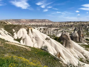 Büyüleyici ve eşsiz doğa ve kaya oluşumunun hava ve panoramik görüntüsü, Kapadokya 'nın peri bacaları, Goreme, Türkiye' nin güzel bir bahar günü mavi gökyüzü, sarı kır çiçeklerinin açtığı