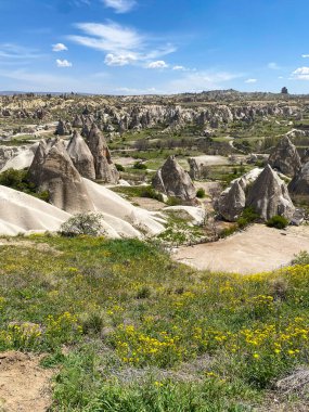 Büyüleyici ve eşsiz doğa ve kaya oluşumunun hava ve panoramik görüntüsü, Kapadokya 'nın peri bacaları, Goreme, Türkiye' nin güzel bir bahar günü mavi gökyüzü, sarı kır çiçeklerinin açtığı