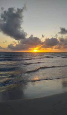 Sahilde parlak bir gün doğumu gökyüzünü ve denizi aydınlatıyor, huzur ve sükunet manzarası yaratıyor..
