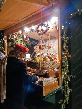 Noel çelenkleri ve çelenklerle süslenmiş, el yapımı süslemeler ve süsler sergilenen bir Noel marketi. Kırmızı bereli bir insan mevsimlik ışıkların arasında alışveriş yapar..