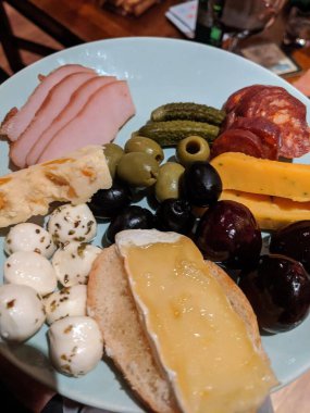 Dilimlenmiş hindi, sucuk, peynirli, peynirli, zeytinli, turşulu ve üzümlü, hafif mavi bir tabakta dizilmiş peynirli bir gurme ve et tabağı..