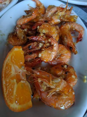 Lezzetli baharatlı ızgara karides kıymalı sarımsak ve beyaz bir tabakta bir dilim taze Galiçya limonu. Tuzlu ve narenciye aromalı canlı bir karışım yaratıyor..