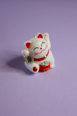 Neşeli bir Maneki Neko biblosu, iyi şansı simgeler, parlak mor bir arka planda zarif bir şekilde oturur