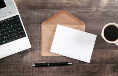 Posta zarfı, kahve, kalem ve dizüstü bilgisayar masanın üstünde..