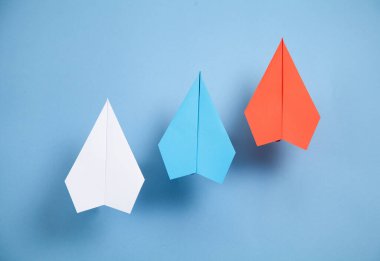 Mavi arka planda kırmızı, mavi ve beyaz kağıt uçaklar. Liderlik. Takım çalışması.