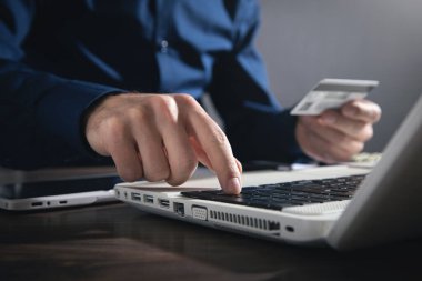 Dizüstü bilgisayar kullanan ve kredi kartı tutan bir iş adamı..