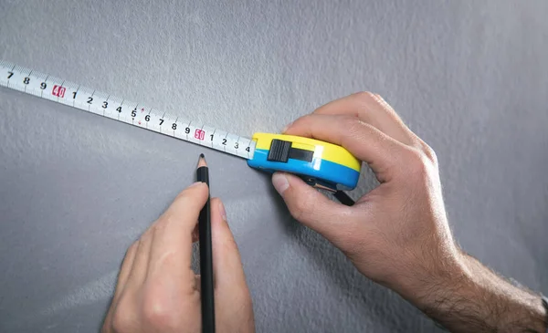 Measuring tape and pencil marking with a wall.