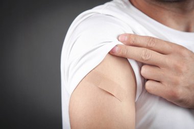 Beyaz bir adam aşıdan sonra omzunu bandajla gösteriyor..