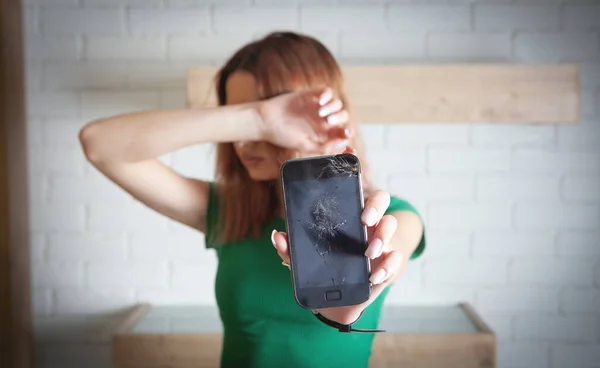 Unhappy young woman holding broken smartphone.