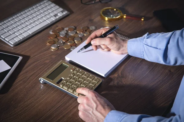 Businessman using calculator and writes in notepad.