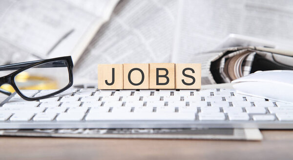 Jobs on wooden cubes with a newspapers and computer keyboard.