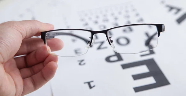 Male hand showing eyeglasses. Eye test chart. Medical eye diagnostic