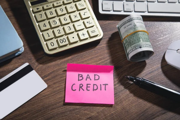 Bad Credit on sticky note with marker, calculator, money.